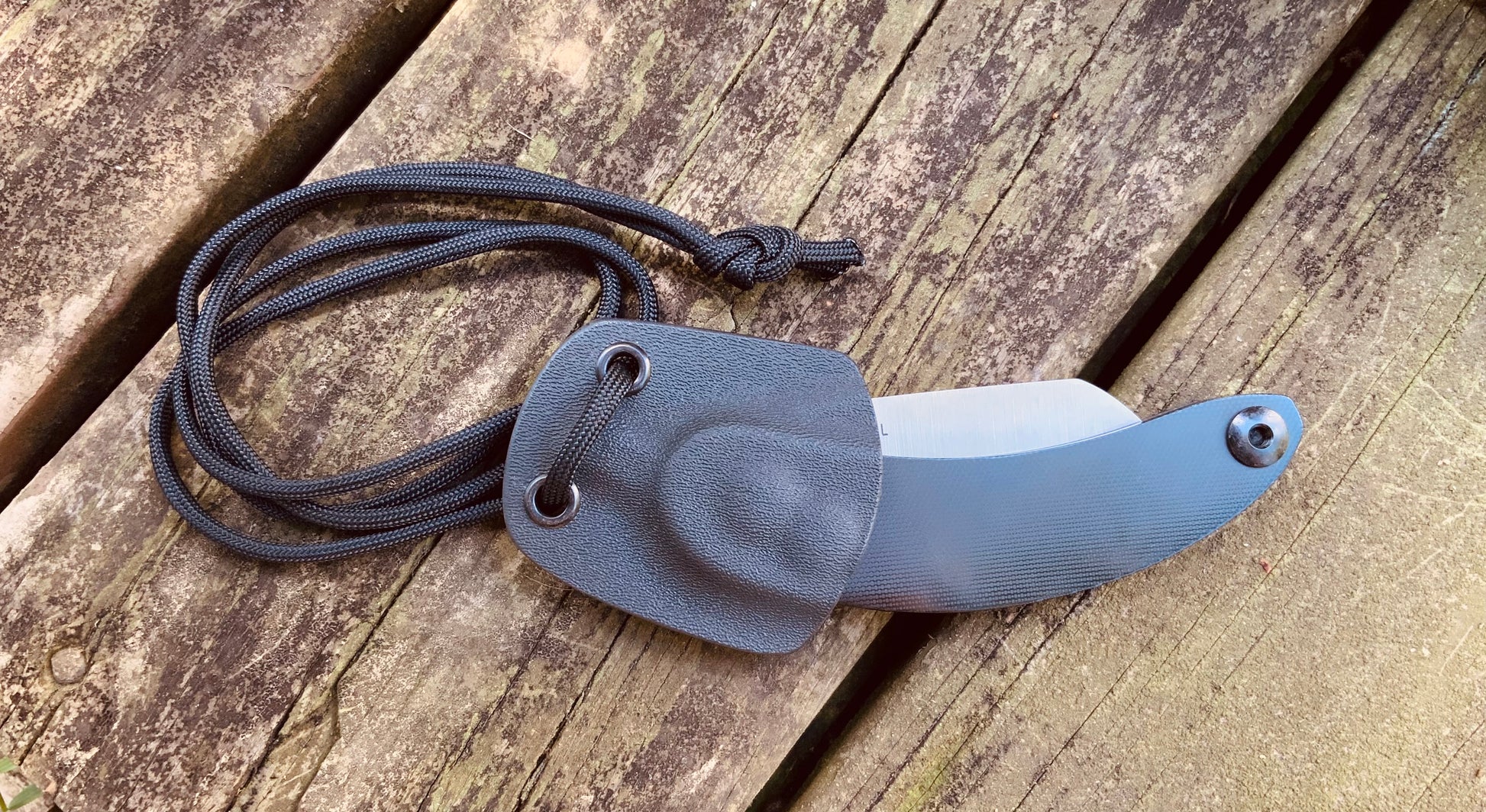 Woods Monkey Neck Knife shown in hand molded Kydex neck knife Sheath with paracord 
